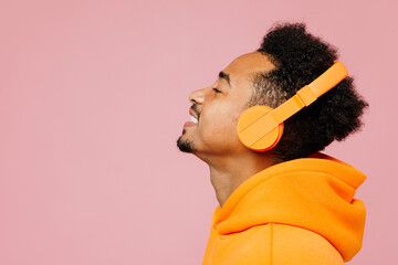 Side view close up young man of African American ethnicity wear yellow hoody casual clothes listen music in headphones isolated on plain pastel light pink background studio portrait Lifestyle concept - obrazy, fototapety, plakaty