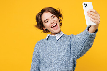 Young woman wears grey knitted sweater shirt casual clothes doing selfie shot on mobile cell phone post photo on social network isolated on plain yellow background studio portrait. Lifestyle concept.