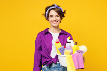 Young smiling cheerful happy woman she wearing purple shirt rubber gloves hold basin with detergent...