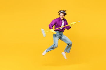Fototapeta na wymiar Full body young fun woman wear purple shirt casual clothes do housework tidy up jump high hold brush broom pov play guitar jump high isolated on plain yellow background studio. Housekeeping concept.