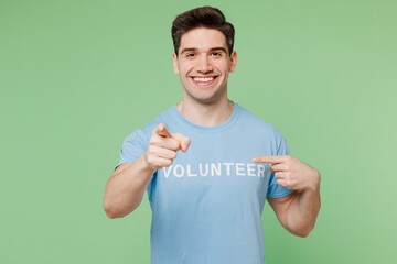Young fun man wears blue t-shirt white title volunteer point index finger on himself camera on you isolated on plain pastel green background. Voluntary free work assistance help charity grace concept.