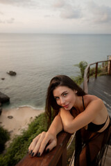 Young pretty brunette woman stand on the balcony of hotel resort with ocean sea view, look at the camera