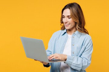 Young smart happy IT woman she wear blue shirt white t-shirt casual clothes hold use work on laptop pc computer chatting online isolated on plain yellow background studio portrait. Lifestyle concept.