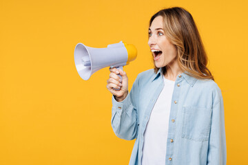 Side view young woman she wears blue shirt white t-shirt casual clothes hold in hand megaphone scream announces discounts sale Hurry up isolated on plain yellow background studio. Lifestyle concept.