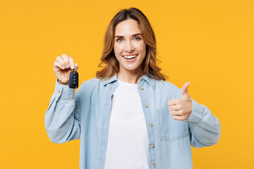 Young smiling happy woman she wear blue shirt white t-shirt casual clothes hold in hand car keys fob keyless system show thumb up isolated on plain yellow background studio portrait Lifestyle concept
