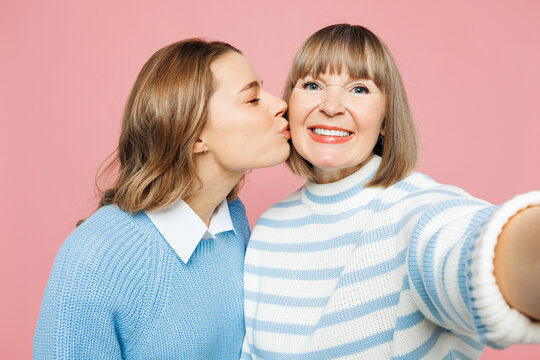 Elder parent mom with young adult daughter two women together wear blue casual clothes do selfie shot pov on mobile cell phone kiss isolated on plain pastel light pink background. Family day concept.