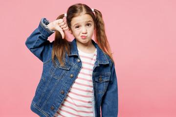 Little dissatisfied sad child kid girl 7-8 years old wears denim shirt showing thumb down dislike gesture isolated on plain pastel light pink background. Mother's Day love family lifestyle concept. - obrazy, fototapety, plakaty