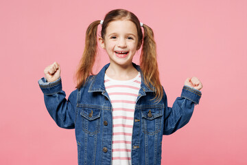 Little child cute kid girl 7-8 years old wears denim shirt have fun do winner gesture celebrate clench fists isolated on plain pastel light pink background. Mother's Day love family lifestyle concept.