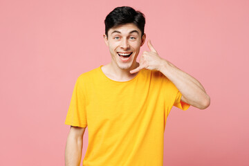 Young surprised happy Caucasian man he wears yellow t-shirt casual clothes doing phone gesture like says call me back isolated on plain pastel light pink background studio portrait. Lifestyle concept.