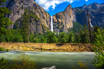 Bridalveil Fall cascading into Yosemite Valley with the Merced River in the foreground in Yosemite...