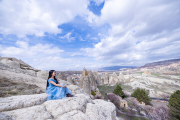 Beautiful woman in blue dress on Turkey rocks mountain.Cheerful woman relax outdoor with beautiful sky and pink flowers in holiday vacation.Woman tourist enjoy amazing mountain view.Travel and freedom