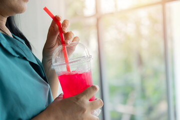 Closeup side view of woman drinking ice red soft drink by straw in the glass.