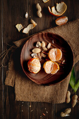 Juicy clementine and peanuts in a wooden plate on a wooden rustic dark table.