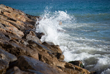 Waves crashing on the rocks in the mediterranean sea at sunset, turquoise water, white foam