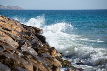Fototapeta na wymiar Waves crashing on the rocks in the mediterranean sea at sunset, turquoise water, white foam