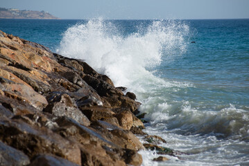 Waves crashing on the rocks in the mediterranean sea at sunset, turquoise water, white foam
