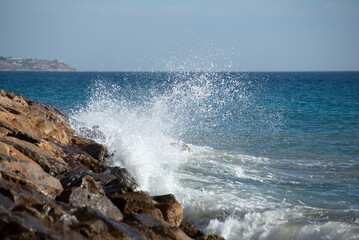 Fototapeta na wymiar Waves crashing on the rocks in the mediterranean sea at sunset, turquoise water, white foam