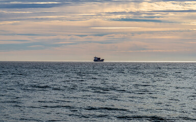 A boat in the distance, in sunset hour of winter season, on the calm waters of the mediterranean sea