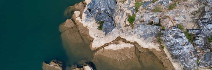 Aerial view of a rugged riverbank with contrasting textures of rock and water, suitable for nature-themed backgrounds with ample copy space