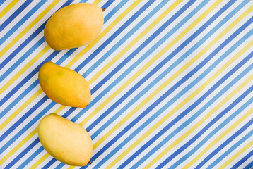 Three ripe mangoes atop a vibrant, diagonal blue and yellow striped background, ideal for summer-themed designs with copy space