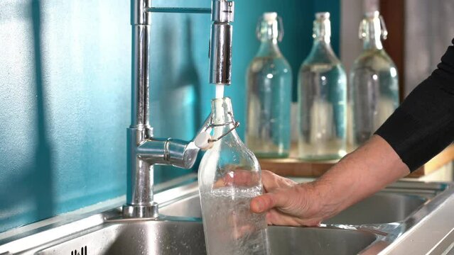 Filling a glass or glass bottle with water from the kitchen tap at home - quality of drinking water in domestic homes. avoid water waste, drought and global warming