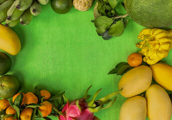 Exotic tropical fruits border on vivid green background with copy space, featuring mango, dragon...