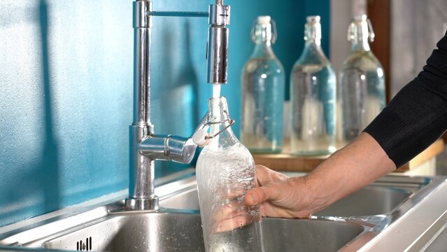 Filling a glass or glass bottle with water from the kitchen tap at home - quality of drinking water in domestic homes. avoid water waste, drought and global warming