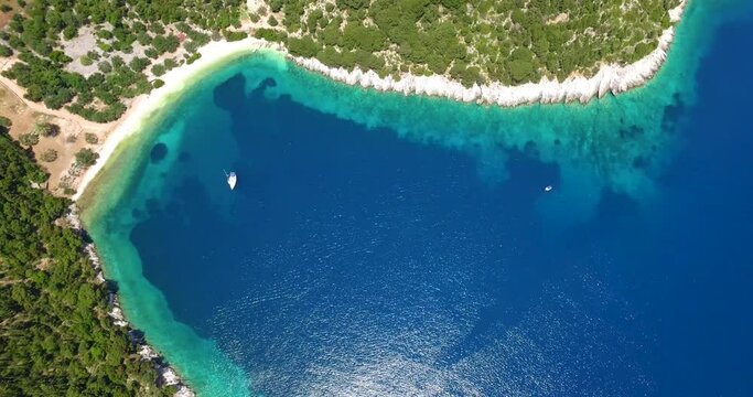 Crystal blue waters edge a lush green cove on Kefalonia Island, aerial view, sunny day