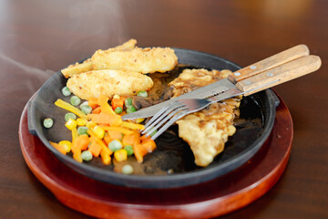 Crispy chicken steak served on hot plate mixed with carrot, potato, and other vegetables