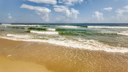Tranquil sandy beach with gentle waves under a blue sky with fluffy clouds, ideal for travel backgrounds with copy space