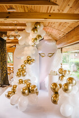 Celebration baptism concept. Trendy cake. Birthday party. Birthday decor for baby party on white background. Photo wall decoration of angel wings and white and gold balloons in hall restaurant.