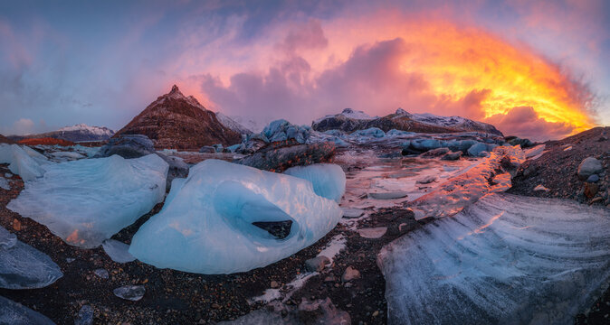 Panoramic view of Svinafell glacier in Iceland with blue ice fragments in the lagoon at sunrise with interesting dramatic orange clouds