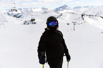 a guy in a ski suit with a helmet and goggles holds skis at the top of the ski slope. winter sport. portrait of a guy with skiing equipment.