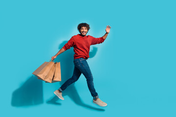 Full length body photo of young shopaholic mexican guy jump raised hand up with packages brand boutique isolated on cyan color background