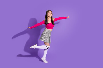 Fototapeta na wymiar Full body photo of carefree cute schoolgirl wear crop top plaid skirt long socks holding arms like wings isolated on violet background