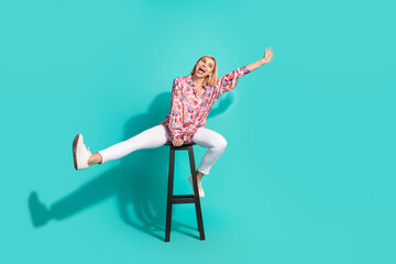 Full body photo of pretty young girl playful have fun sit chair dressed stylish pink print outfit isolated on aquamarine color background