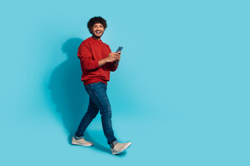 Fototapeta na wymiar Full length body photo of mexican funny man laughing when strolling using smartphone texting girlfriend isolated on blue color background