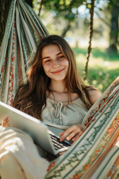 Smiling young woman relaxing on hammock with tablet in sunny park