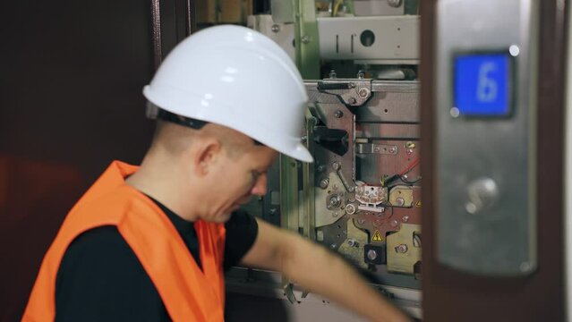 A utility worker is repairing the equipment of a passenger elevator. The elevator doors are open and the engineer is adjusting the automatic lift system.