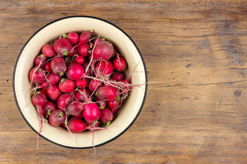 ripe red radishes in a yellow enameled bowl on an old wooden table top view with a copy space - 747934312
