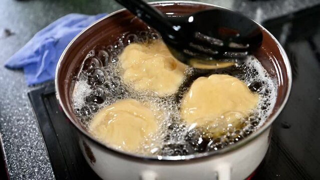 Berliner or doughnut cooking traditionally at home in a pot, close-up in slow motion. Add new dough. Boil oil and fat, hot temperature with bubbling 