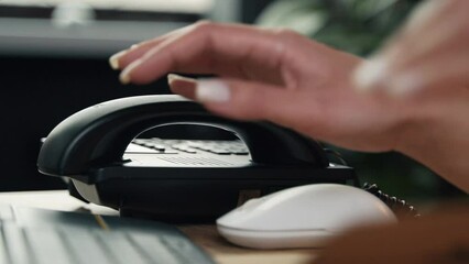 A close-up shot of a female office worker picking up the phone to answer a phone call whilst working at his desk.