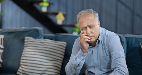Asian India retired old elder gen x tired upset sad man sitting alone sofa couch feel bad sorrow...