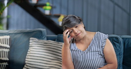 Asian Indian gen x older adult tired sad lady sitting alone sofa couch feel bad indoor home elder...