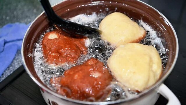 Turning Berliner or doughnut while cooking traditionally at home in a pot, close-up in slow motion. Boil oil and fat, hot temperature with bubbling 