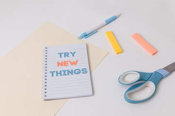 Notebook with Try new thing text is on top of white office desk table with blue pen, scissors,...