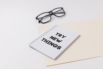 Notebook with Try new thing text is on top of white office desk table with black glasses