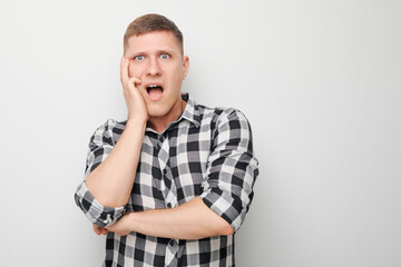Shocked man with hand on cheek standing against white background expressing surprise and disbelief