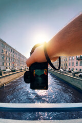 male hand holding a camera against the a river between old buildings to take a picture, pov, point of view perspective