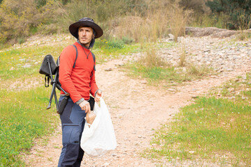 mountaineer with hat picking up garbage in nature.